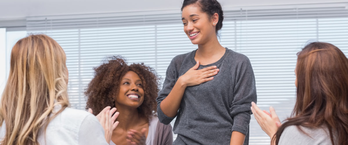 Happy patient has a breakthrough in group therapy while others are clapping her